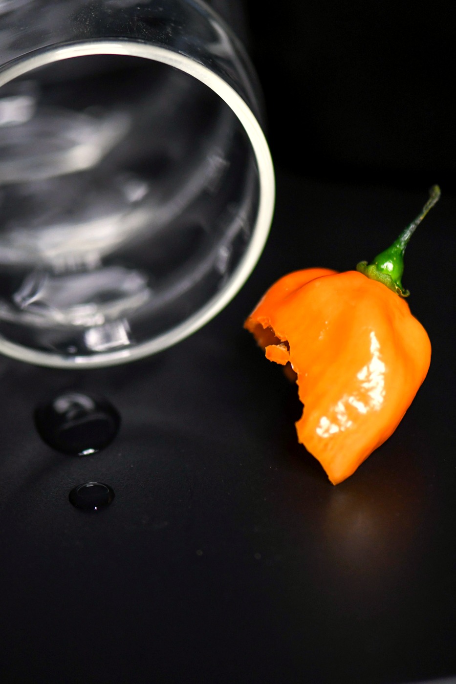 A habanero pepper beside a glass jar on black